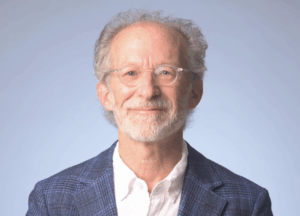 Headshot image of Rick Summers against a light grey backdrop. Rick is wearing a white button down and gray-blue suit jacket.